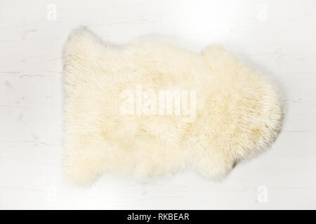 Flat lay view of white warm and cozy whole real decorative sheepskin rug on white wooden board floor.  Room for text. Studio set. Stock Photo