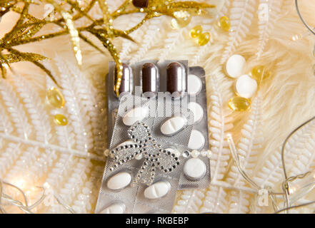 Top view of different pills vitamins as a Christmas gift idea concept on white fluffy lambskin with white decorative leaves and party lights. Recoveri Stock Photo