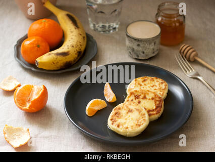 Vegetarian breakfast of quark pancakes with honey, fruit and coffee with milk. Rustic style. Stock Photo