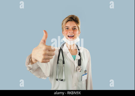 Young doctor girl shows thumb up on blue isolated background. Concept medicine and health Stock Photo