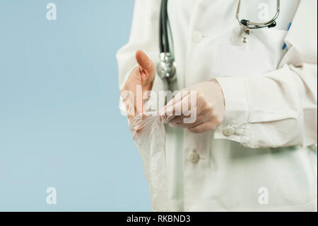 The doctor puts on gloves close-up on an isolated blue background. Concept medical clothes Stock Photo