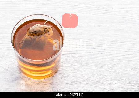 Tea bag in a glass transparent cup with hot water on a white wooden table Stock Photo