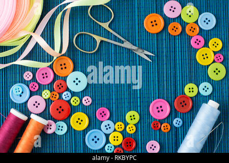Tailoring equipment: many colorful buttons, threads, ribbons, scissors and a needle on a dark blue straw mat - text space Stock Photo