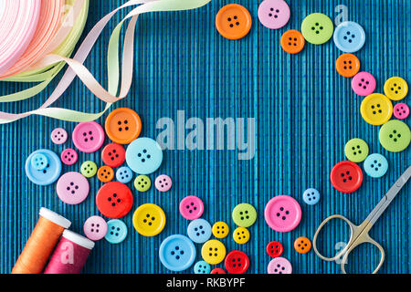 Tailoring equipment: many colorful buttons, threads, ribbons, scissors on a dark blue straw mat - text space Stock Photo