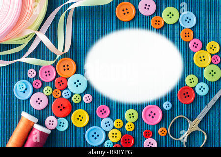 Tailoring equipment: many colorful buttons, threads, ribbons, scissors on a dark blue straw mat - white oval text space Stock Photo