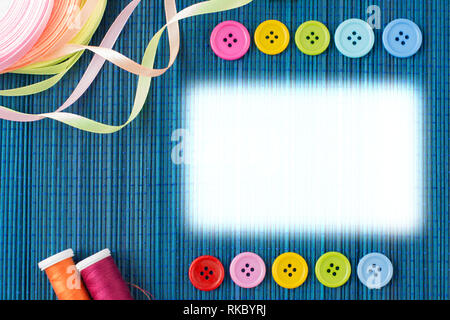 Tailoring equipment: two rows of colorful buttons, threads and ribbons on a dark blue straw mat - white rectangular text space Stock Photo