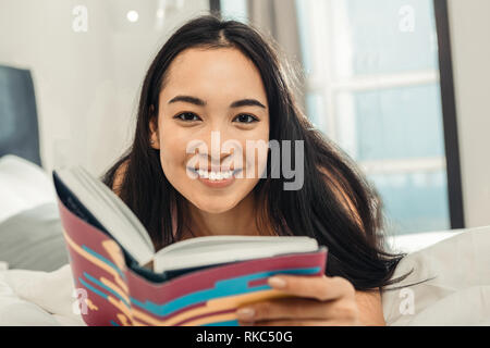 Beautiful dark-eyed woman smiling broadly while reading book Stock Photo