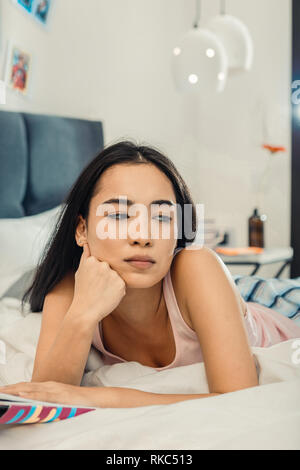 Dark-eyed woman feeling bored and lonely after reading book Stock Photo