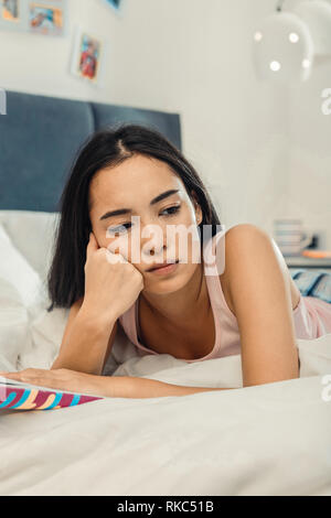 Dark-eyed woman feeling sad and lonely lying in her bedroom Stock Photo