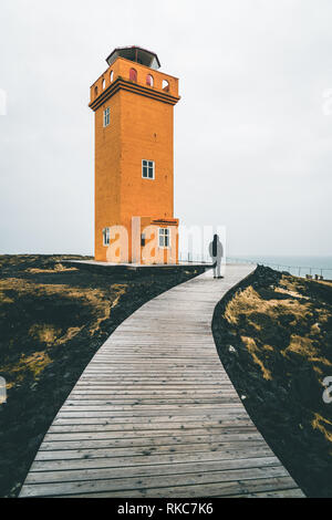 Unidentified Person standing in front of Orange Lighthouse Svortuloft Skalasnagi tower in Snaefellsnes Peninsula, west Iceland on an overcast day. Stock Photo