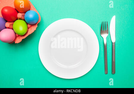 Easter table, place setting. Easter eggs, pastel colors painted, empty white plate, green background, copy space, top view Stock Photo