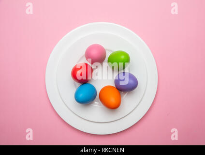 Easter eggs, pastel colors painted in a white plate, pink color background, top view Stock Photo