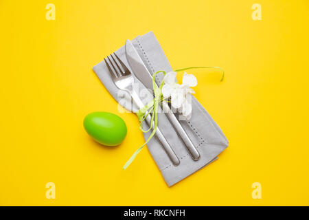 Easter table, place setting. Easter egg, green color painted, cutlery and grey napkin, yellow background, top view Stock Photo