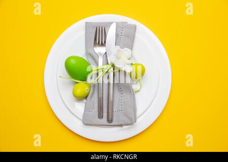Easter table, place setting. Easter eggs, green color painted in a white plate, yellow background, top view Stock Photo