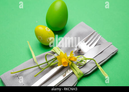 Easter table, place setting. Easter eggs, painted, cutlery and grey napkin, green color background, close up view Stock Photo