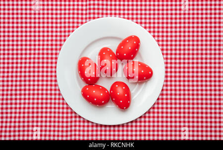 Easter eggs, red with dots, in a white plate, red checkered tablecloth background, top view Stock Photo