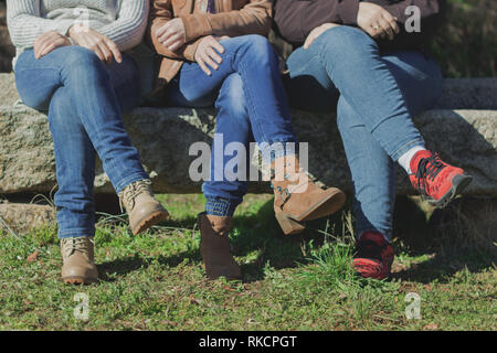 Women sitting cross-legged on a stone bench with jeans, in the field Stock Photo