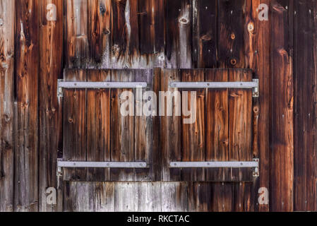Closed window shutter of wood in a wood panel wall of alpine outbuilding with distinctive metal hinges Stock Photo