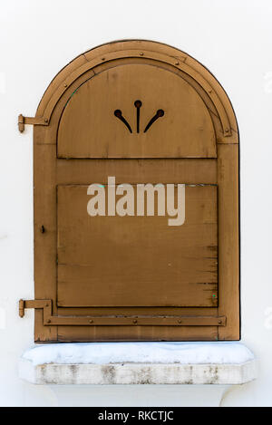 Bespoke dilapidated wood window shutter in arched window on white stone wall in winter Stock Photo