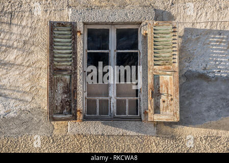 Weather-worn dilapidated open window shutters on render stone building casting shadows on wall Stock Photo