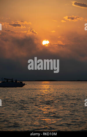 Boat on ocean, Bright sun in an orange sky with dark clouds at sunset, France Stock Photo