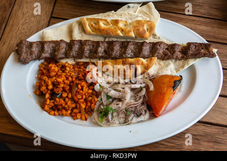 Turkish Adana kebab with bulgur cereals and bread, lavash and onions. Stock Photo