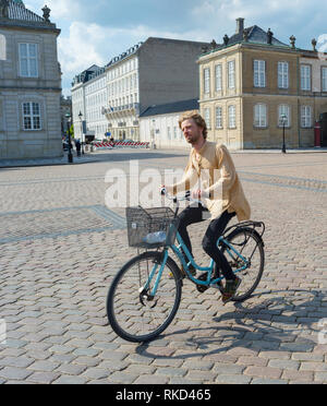 COPENHAGEN, DENMARK - JUNE 14, 2019:  Young hipster man riding city bicycle in bright sunshine at Amalienborg Palace Square, Copenhagen, Denmark, Euro Stock Photo