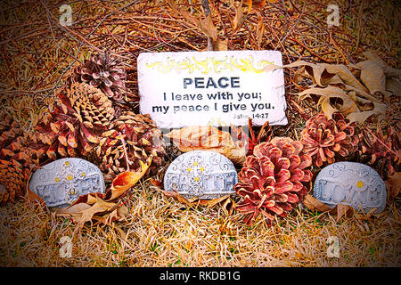 Close-up of several pinecones on the ground with leaves, vines, a quote from the Bible, and three handcrafted stones that have symbols on them and the Stock Photo