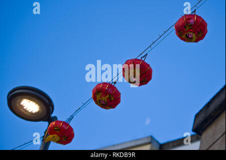 Stock picture of four red Chinese lanterns hanging on wire across a lamp post against a blue sky with moon slightly visible on bottom right. Stock Photo