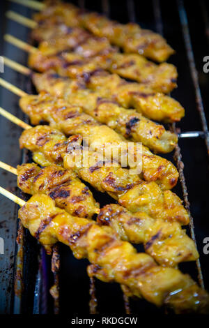 Chicken satay on bamboo skewers cooking on a grill in a Thai market stall.  Satay is a dish of seasoned, skewered and grilled meat, served with a sauc Stock Photo