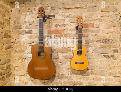 Two acoustic guitars hanging on brick wall background indoors. Vintage retro style Stock Photo