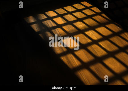 Dark window bars shadow on the wooden floor in prison Stock Photo