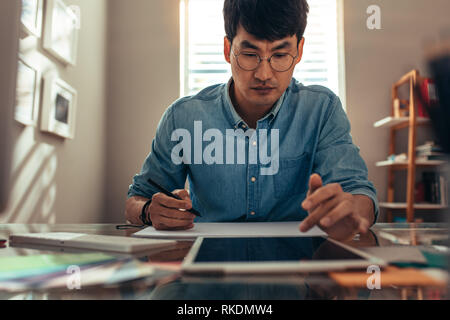 Creative man working in office with tablet pc and dawning book. Male interior designer making a drawing on book while taking reference from digital ta Stock Photo