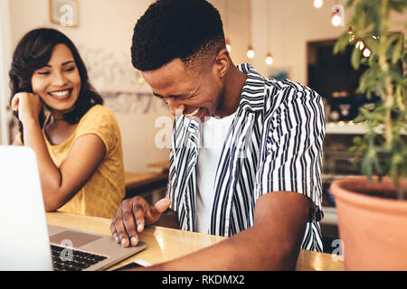 Young man smiling while talking with female friend at coffee shop. Two young creative people meeting at cafe. Stock Photo