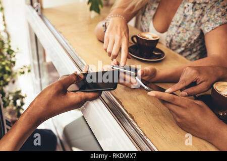 Cropped shot of young people connecting their devices at coffee shop. Close up of friends using Wi-Fi to connect each other's mobile phones. Stock Photo