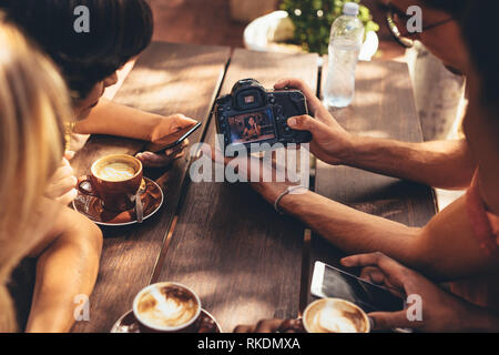 Man showing a picture on his dslr camera to friends sitting at cafe table. Group of creators meeting at cafe and looking at content. Stock Photo