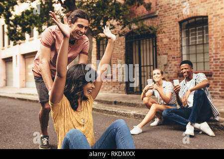 Group of friends creating new social media content outdoors. Young people taking pictures with mobile phones of couple having fun on skateboard on cit Stock Photo