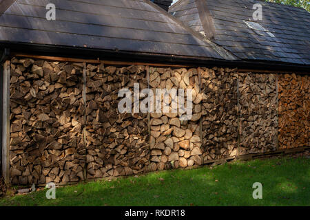 Piles of tree logs as firewood material by barn wall as home self sufficient energy in rural Ireland, Killarney, County Kerry Stock Photo