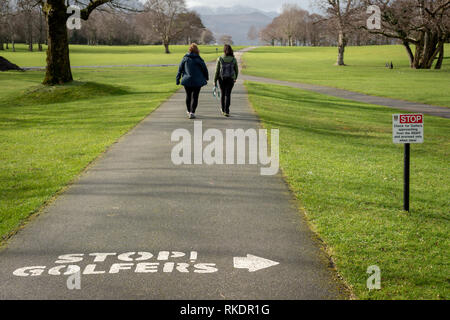 Two women walking on golf course alley by golf course rules information sign in Killarney Golf and Fishing club in Killarney, County Kerry, Ireland. Stock Photo