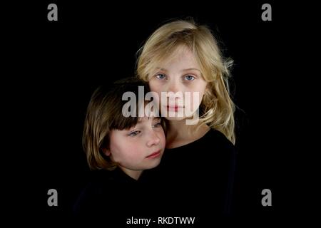 Closeup of two young sisters grieving and holding each other against a black background Stock Photo