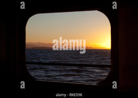 View of the Vancouver city skyline at sunrise with background clouds seen off the coast through a porthole on a ferry in the Georgia Straight Stock Photo
