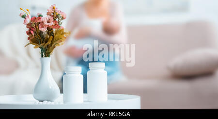 close-up view of containers with pills, flowers in vase and mother breastfeeding baby behind at home Stock Photo