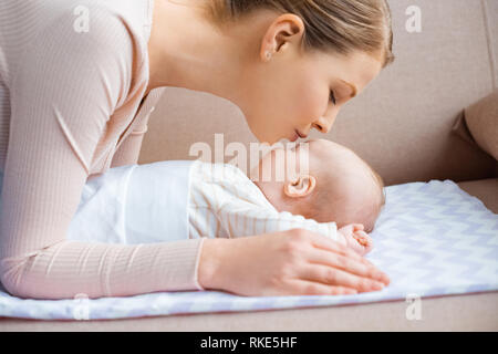 side view of happy young mother kissing adorable child lying on couch