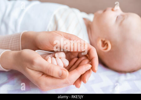 cropped shot of mother holding hand on adorable infant baby lying on sofa