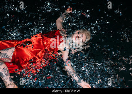 blonde woman lying on floor with confetti isolated on black Stock Photo