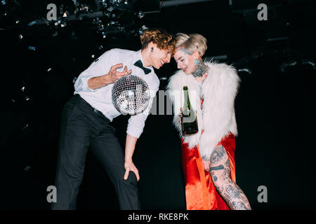 man holding disco ball and standing near woman with bottle of alcohol drink on party on black background Stock Photo