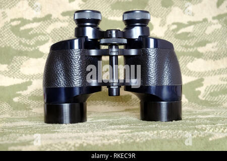 Vintage Porro prism black color military binoculars on camouflage background front view close up Stock Photo