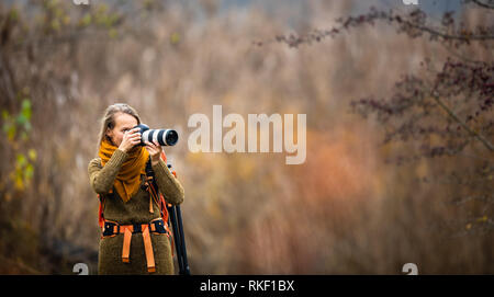 Pretty, female photographer taking pictures outdoor on a lovely autumn day - shallow DOF, color toned image