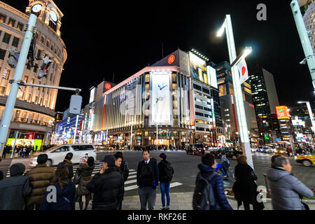 Tokyo, Ginza, night. Wide angle view of people waiting at pedestrian crossing, Wako and Mitsukoshi department stores opposite. Traffic, motion blur. Stock Photo