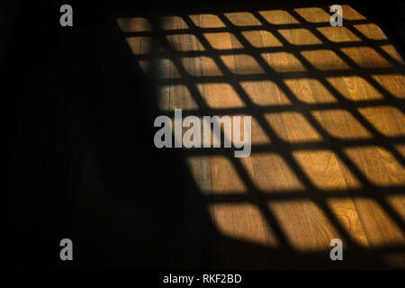 Dark window bars shadow on the wooden floor in prison Stock Photo